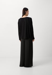 Blusa nera con una vestibilità morbida, scollatura rotonda sul retro e spalle arricciate, abbinata a pantaloni neri larghi e fluidi. Tessuto di superficie liscia.