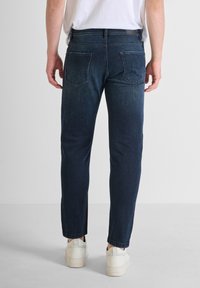 Jeans de mezclilla azul oscuro con corte recto, diseño de cinco bolsillos y costuras blancas. Presentan una cintura estándar y un corte a la altura de los tobillos.