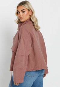 Ljust rosa, oversized denimjacka med hög krage, fransad fåll och två framfickor. Texturerad tyg med avslappnad passform.
