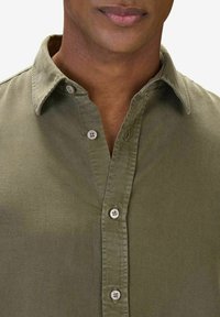 Harmaa vihreä nappipaita, joka on valmistettu puuvillakankaasta. Paita on varustettu terävällä kauluksella ja valkoisilla napituksilla, ja sillä on sileä, teksturoitu pinta.