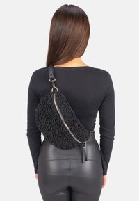 Schwarze, strukturierte Schultertasche aus plush Material mit silbernem Reißverschluss und Ledertragegurt, die eine kurvige Form und nahtloses Design aufweist.