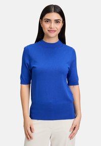 Maglietta a maniche corte in maglia blu con collo a giro, texture liscia e design aderente. L'orlo e i bordi delle maniche sono a costine per un tocco di dettaglio in più.