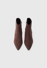 Botas de tornozelo em camurça castanha com bico fino, apresentando um fecho éclair preto no lado externo e uma sola preta lisa.