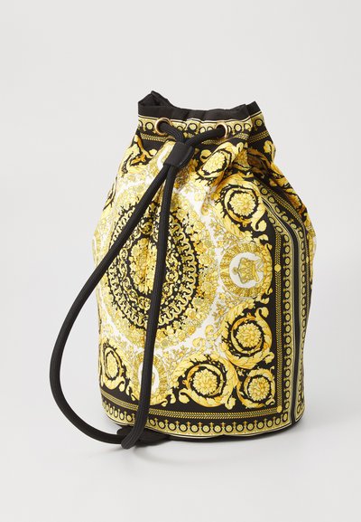 Sac seau à cordon en tissu noir et blanc avec des motifs floraux jaunes ornés et des accents en métal doré. Texture lisse avec une forme décontractée.