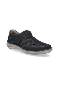 Sorte ruskind slip-on sko med udskårne detaljer, kontrasterende beige sting og gummisål. Brune læderdetaljer ved hælen.