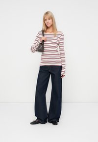 Top à manches longues rayé en blanc, bordeaux et marine ; associé à un pantalon en denim foncé à jambes larges. Les accessoires comprennent un petit sac à main gris et des chaussures noires.