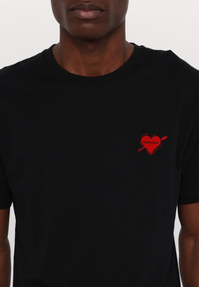 Černé tričko s krátkým rukávem vyrobené z bavlny, s grafickým motivem červeného srdce s šipkou a nápisem "THE KOOPLES" na levém prsu.