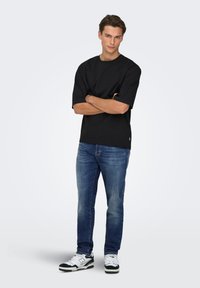 T-shirt en coton noir à manches courtes, col rond et coupe droite, associé à un jean en denim bleu et des baskets noires et blanches.