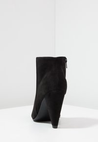 Musta mokka nilkkuri, jossa on terävä kärki ja korkea stiletto-korko. Varustettu takakautta avautuvalla vetoketjulla ja sileällä, mattapinnalla.