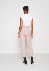 Vit ärmlös topp och ljusrosa skräddarsydda byxor med hög midja, fickor och rak bendesign. Svarta ankelstövlar fulländar looken.