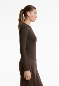 Barna, hosszú ujjú felső kerek nyakkivágással és testhez simuló sziluettel, bordázott textúrával és oldalsó varrás kiemelő részletekkel.
