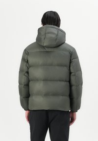 Groene gewatteerde jas met capuchon, voorzien van een gestikt ontwerp, elastische boorden en een soepele textuur. Zichtbare stiksels en effen kleur.