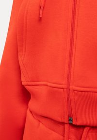 Sweat à capuche zippé rouge vif avec taille côtelée, capuche à cordon de serrage et détails de couture sur la poche avant.