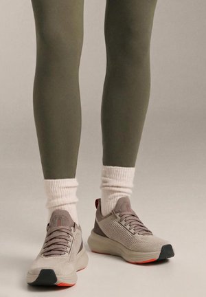 Light gray athletic shoes with textured fabric, laces, and a black toe cap, paired with olive leggings and cream socks.