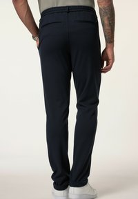 Navy Jogginghosen mit einem Kordelzugbund, schmal zulaufenden Beinen und zwei Gesäßtaschen, kombiniert mit weißen Sneakern. Glatter Stofffinish.