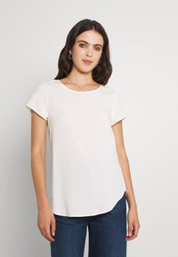 Hvit kortermet bluse med rund hals, myk tekstur, avrundet nederkant og en avslappet passform, kombinert med blå denimjeans.