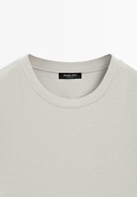 Lyse beige t-shirt med rund hals og en Massimo Dutti-label syet ind på indersiden af nakken.