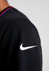 Schwarzes Sportshirt mit einer engen Passform, rundem Halsausschnitt mit roten und lila Akzenten und einem auffälligen weißen Nike-Logo am Ärmel.