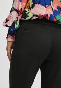 Black trousers with a smooth texture, featuring a back pocket. The flowy top has a floral pattern in pink, blue, and green hues.