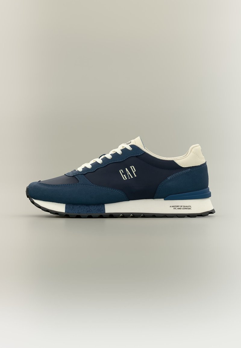 Σκούρα μπλε και λευκό αθλητικό παπούτσι GAP με λευκά κορδόνια, μαλακή σόλα και λογότυπο στο πλάι και τη φτέρνα, εμφανιζόμενο σε προφίλ σε ουδέτερο φόντο.