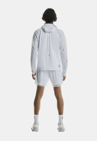 Haut de sport blanc avec capuche à cordon, associé à un short assorti. Tissu lisse et accents de logo discrets.