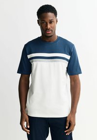 Korte mouw T-shirt met een marineblauwe bovenkant, een wit lijf en horizontale strepen in marineblauw en grijs over de borst. Gemaakt van een katoenmix.