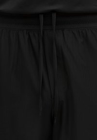 Pantalones cortos deportivos negros con una cintura elástica que presenta una banda texturizada, ajustados con cordones planos para un ajuste seguro.