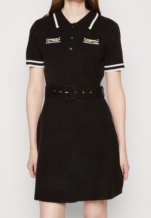 Czarna sukienka z krótkim rękawem, z białą lamówką na kołnierzyku i rękawach, zapięcie na złote guziki, ozdobne złote akcenty na piersi oraz pasujący czarny pasek.