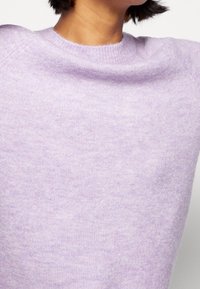 Laventelinvärinen neulepaita, jossa on sileä pinta, pyöreä pääntie ja istuva leikkaus. Kangas näyttää pehmeältä ja siinä on hienovarainen meleerattu kuvio.