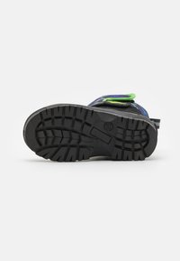 Schwarze, langlebige Gummisohle mit strukturiertem Griffmuster. Verfügt über verstellbare grüne und blaue Riemen auf einem mehrfarbigen Oberdesign.