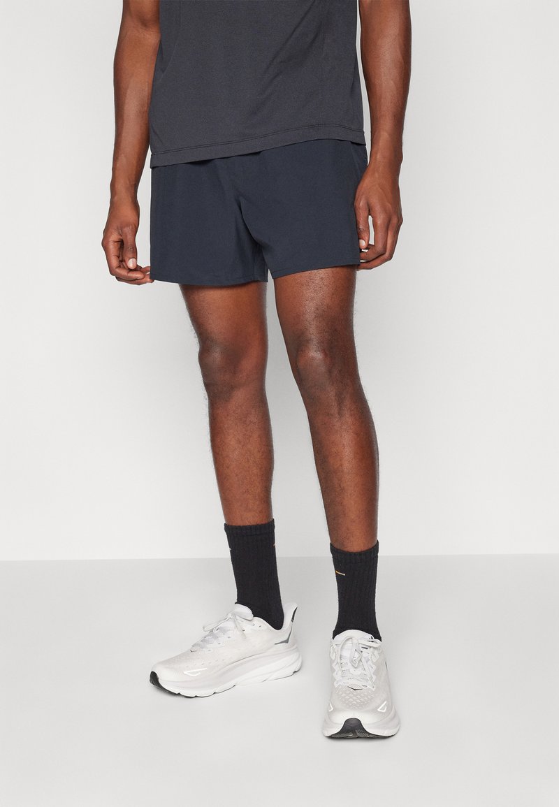 Marinblå sporty shorts med en løs pasform, parret med en mørk t-shirt og hvide løbesko. Indeholder sorte sokker med diskrete detaljer.