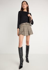 Fekete hosszú ujjú felső bézs kockás rakott szoknyával, széles övvel, kiegészítve fényes fekete térdihúzó stiletto csizmával.