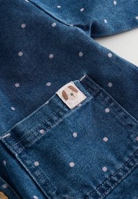 Jeans-Latzhose aus blauer Baumwolle mit hellrosa Punkten und einer rechteckigen Tasche, die mit einem süßen Hundegesicht bestickt ist.