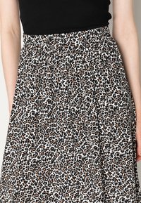 Jupe en imprimé léopard avec une taille élastique noire, présentant un mélange de couleurs noir, marron et crème, fabriquée en tissu léger.