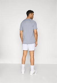 Hallhalli halli T-särk lühikeste varrukatega, siledast materjalist ja ümar kaelus, koos valgete lühikestega. Tagantvaates on minimalistlik disain.