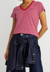 Personne portant un T-shirt rayé rouge et blanc à col en V avec une veste en jean foncée nouée autour de la taille.