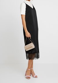 Černé šaty na ramínka s krajkovým lemem, vrstvené přes bílé tričko s krátkým rukávem. Doplněné zlatou kabelkou přes rameno a růžovými sandály na podpatku.