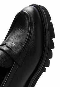 Zwarte leren schoen met een gemêleerde afwerking, in moccasinstijl, met decoratieve stiksels en een robuuste, geprofileerde zool.