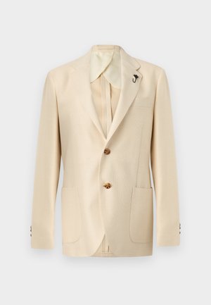 Beige herreblazer med hakket revers, to brune knapper, to forlommer med påsyede lommer og en lille reversnål på en ensfarvet baggrund.