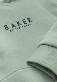 Felpa verde chiaro con scollatura rotonda, polsini a costine e la scritta "BAKER by TED BAKER" stampata in bold nero. Texture del tessuto morbida.