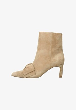 Beige Wildleder-Ankle-Boot mit spitzer Zehe, einer dekorativen Schleife an der Seite und einem schlanken Absatz. Glatte Textur mit einem subtilen Glanz.