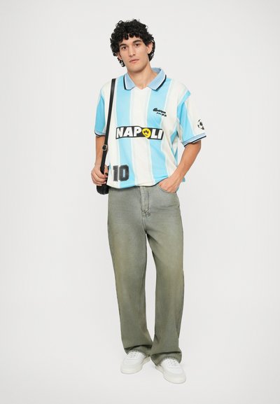 Polo shirt à rayures bleu clair et blanches avec un logo noir "NAPOLI" sur le devant et le numéro 10, associé à un jean gris délavé ample et des baskets blanches.