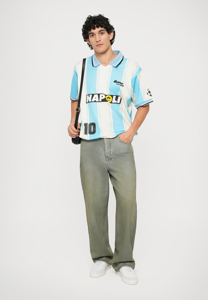 Light blue and white striped polo shirt with black "NAPOLI" logo at the front and number 10, paired with loose, faded grey jeans and white sneakers.