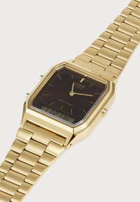 Ρολόι quartz χρυσού τόνου Casio με ορθογώνιο πρόσωπο, μαύρο καντράν, αναλογ ικές δείκτες και ψηφιακή οθόνη. Μεταλλικό βραχιόλι με κούμπωμα και υφή στα links.