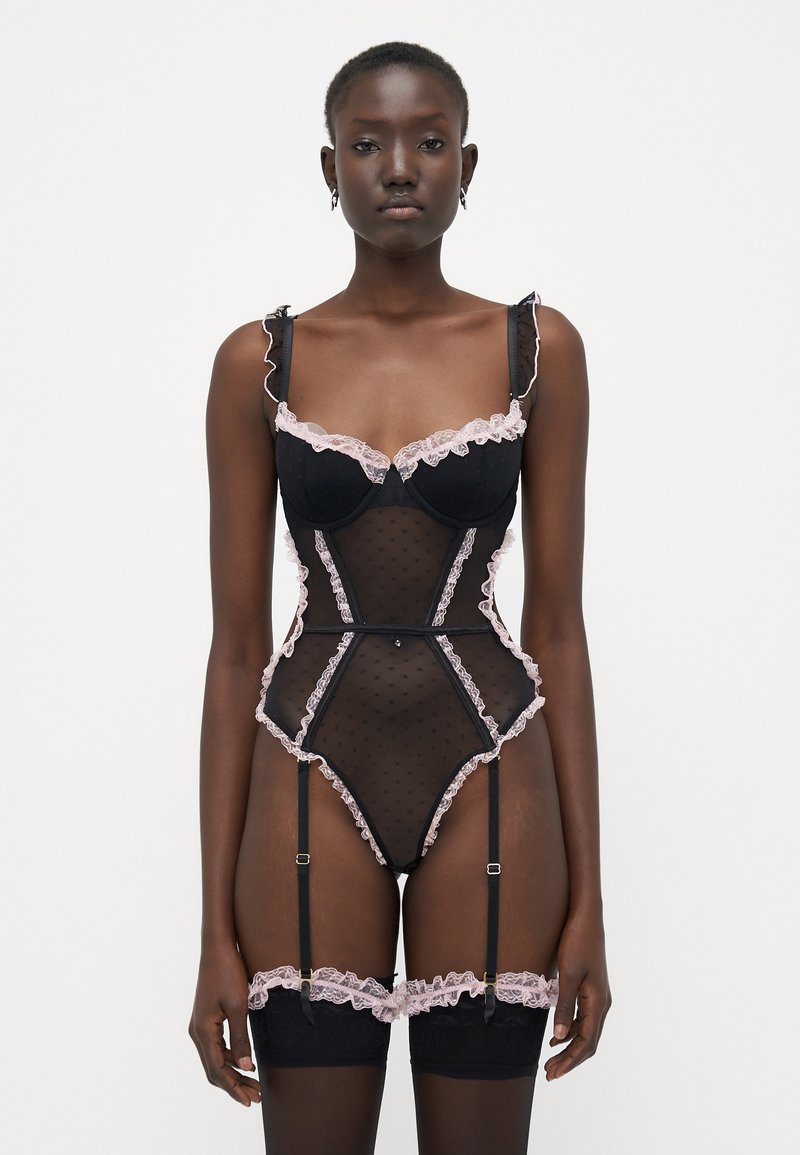 Lingerie nera con motivi a pois e dettagli in pizzo rosa. Presenta spalline arricciate, un design aderente e dettagli con reggicalze. Tessuto testurizzato.