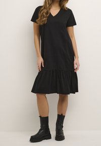 Czarna bawełniana sukienka z krótkimi rękawami, dekoltem w kształcie litery V i falbaną na dole. Połączona z czarnymi botkami do kolan. Gładka tekstura, luźny krój.