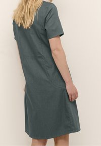 Vestido corto de manga corta en gris oscuro, confeccionado en tejido suave, que presenta un corte relajado con dobladillo redondeado y bolsillos laterales, mostrando un diseño simple y clásico.