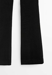 Jambes de pantalon en tissu côtelé noir avec un ourlet droit sur fond blanc, montrant la texture et les détails de couture.