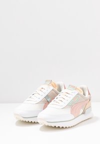 Baskets blanches avec des accents pastel en rose, menthe et pêche. Caractérisées par un mélange de matériaux lisses et texturés, une semelle coussinée et une fermeture à lacets.