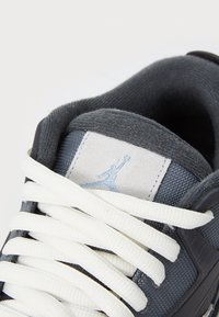 Gros plan sur une basket gris foncé avec des lacets blancs et une languette gris clair ornée d'un logo Jumpman bleu clair.